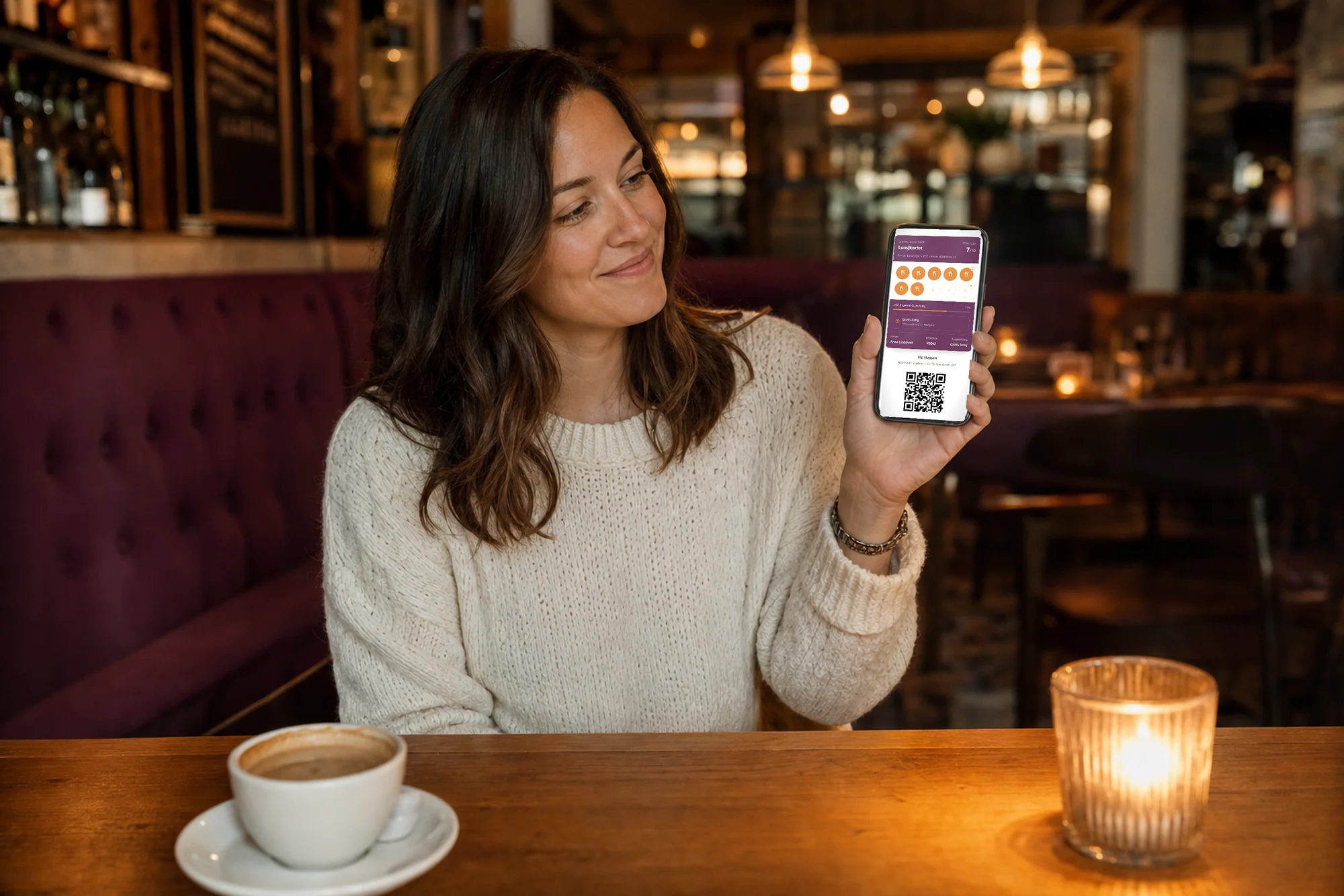 Gjest ved bordet i en varm bistro viser det digitale stempelkortet i mobilen — sju av ti stempler i lunsjkortet og en QR-kode å skanne ved kassen