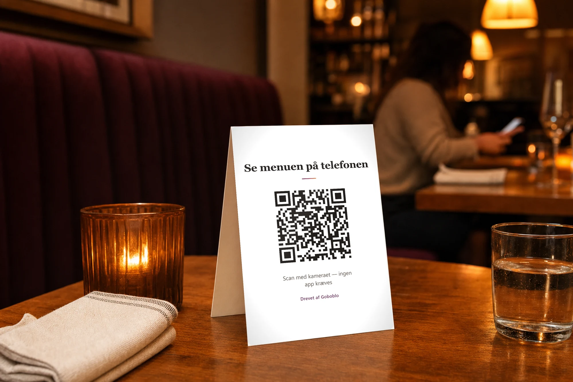 Bordskilt på et restaurantbord med en ægte QR-kode — Se menuen på telefonen, scan med kameraet, ingen app kræves — i varmt aftenlys