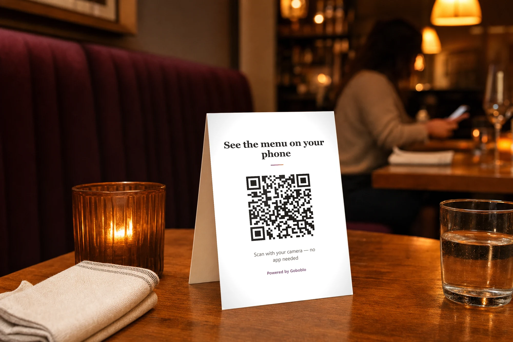 Table tent on a restaurant table with a real QR code — See the menu on your phone, scan with your camera, no app needed — in warm evening light