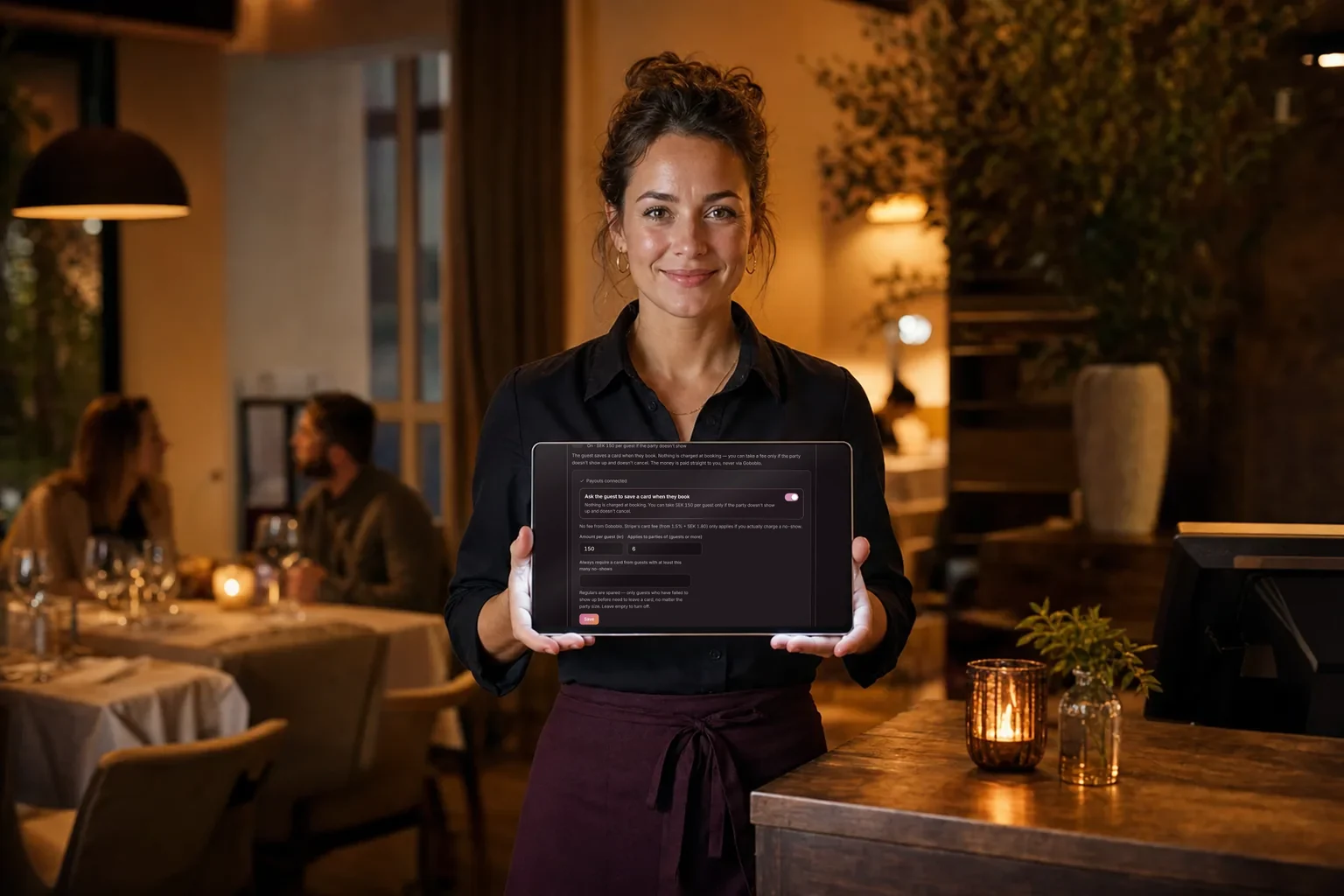 Restaurant manager holding a tablet with Goboblo's no-show protection in English – the card-on-file setting with the amount per guest